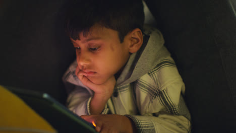 Close-Up-Of-Young-Boy-In-Home-Made-Camp-Made-From-Cushions-Playing-With-Digital-Tablet-At-Night-2